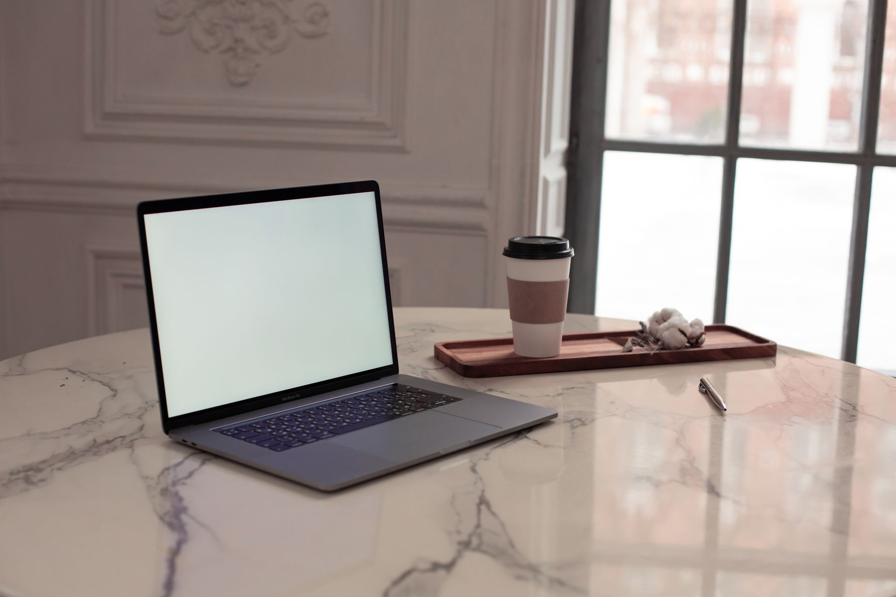 A laptop and a cup of coffee on a marble desk by a window